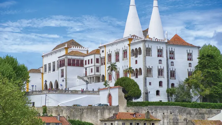 Hilltop palace of white walls topped by two huge white conical kitchen chimneys, set against a blue sky above terracotta rooftops