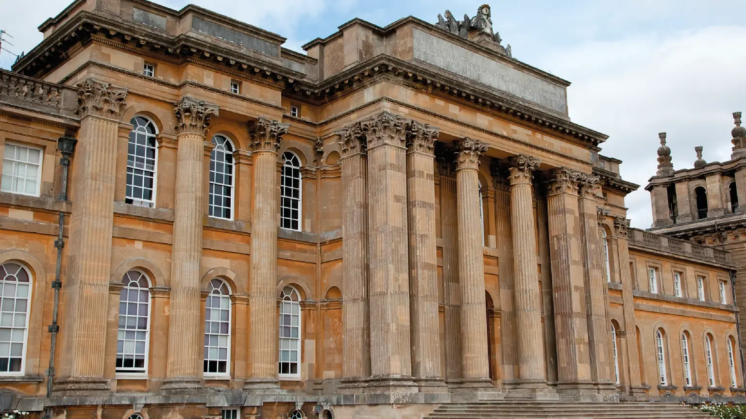Vast English baroque palace with grand colonnaded courtyard and classical statues, set in landscaped parkland