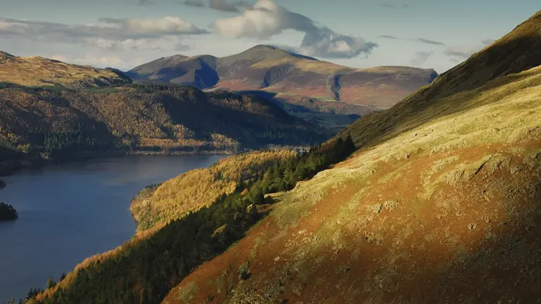 Calm lake reflecting wooded fells and dramatic mountain scenery typical of the English Lake District