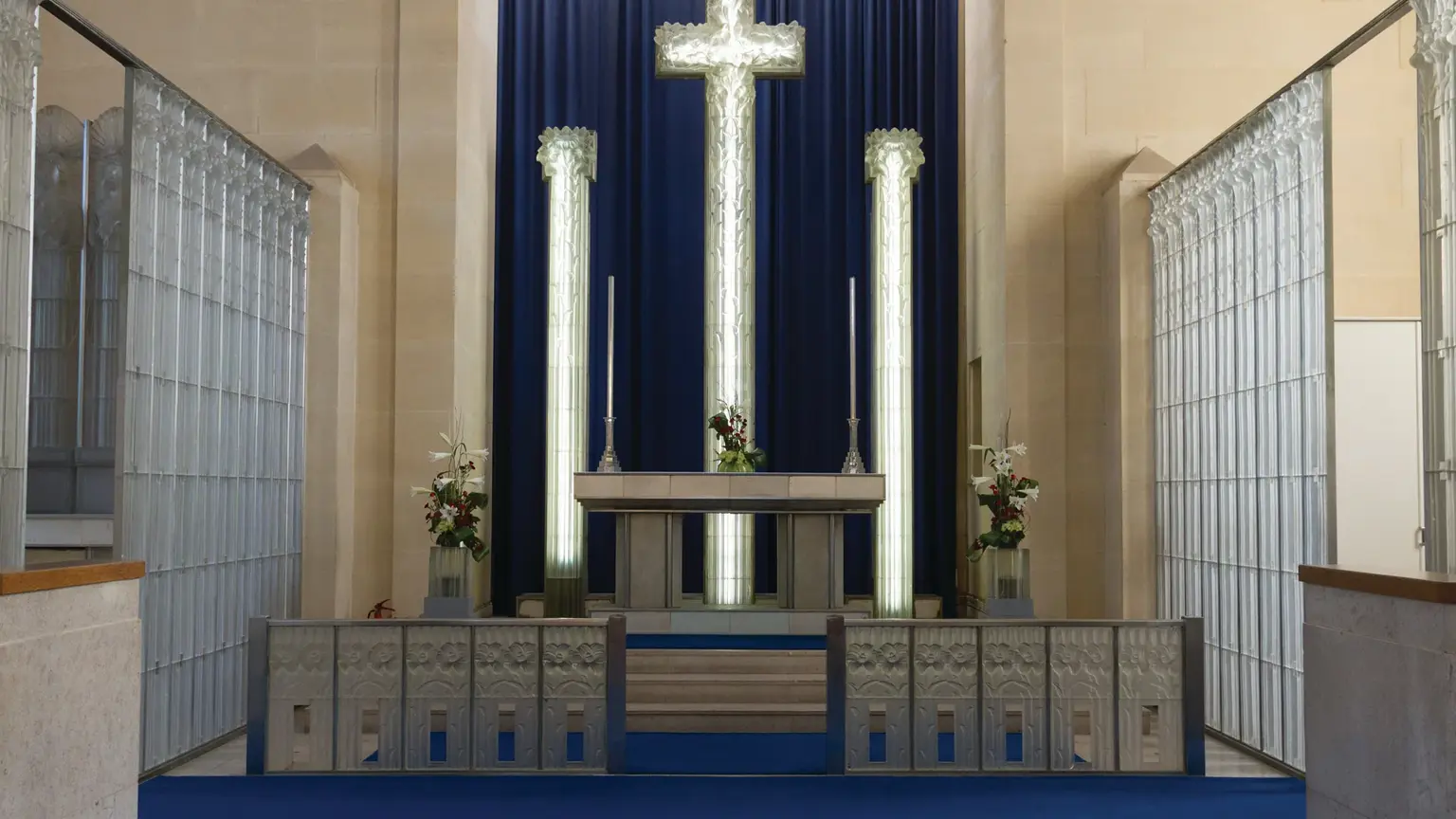 The illuminated Lalique glass altar cross at St Matthew's Church Millbrook, flanked by glowing glass screens and pillars in a deep blue interior