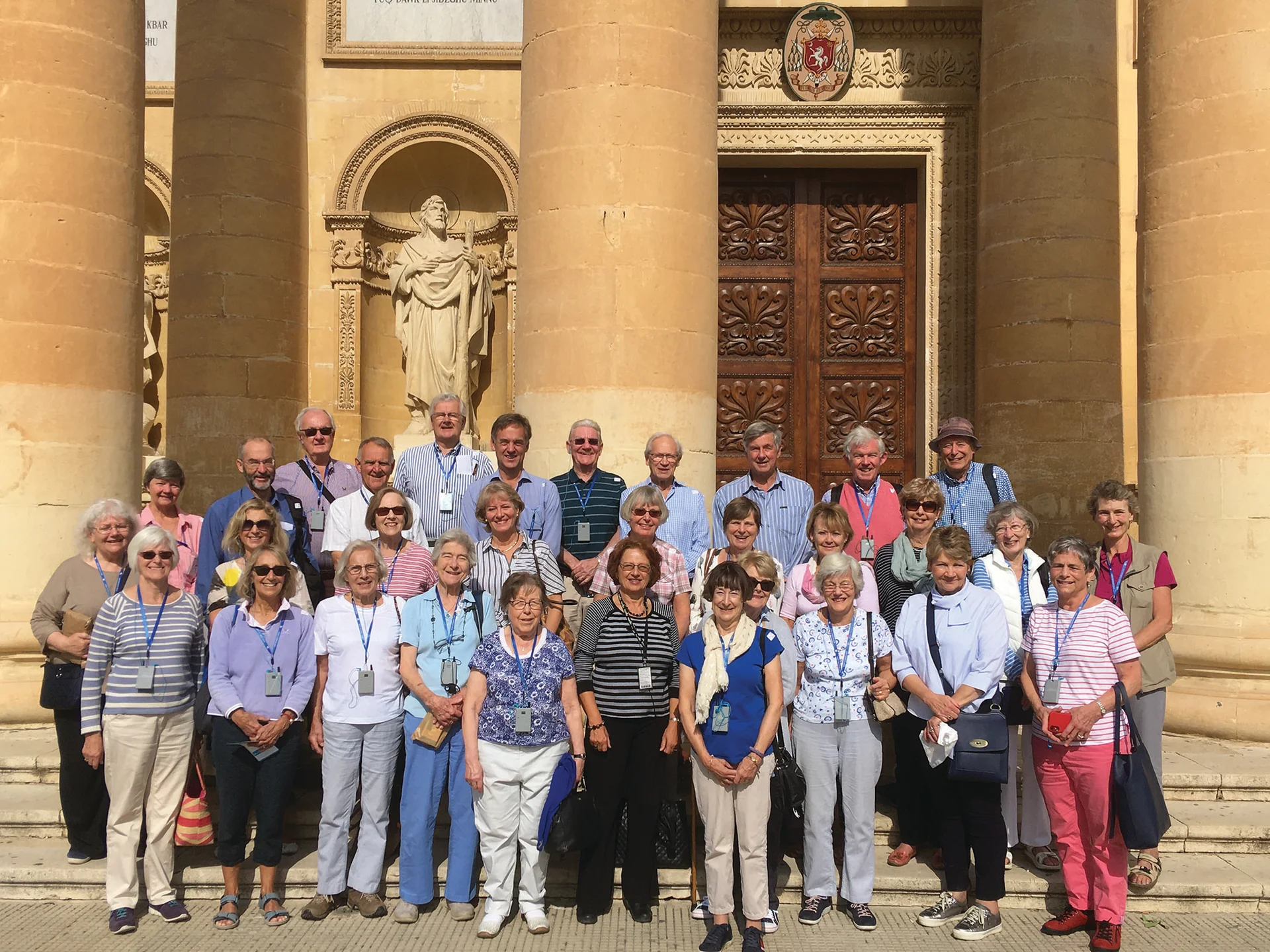 Group of visitors posed outside the Church of St Mary in Mosta, Malta, featuring its iconic domed structure.