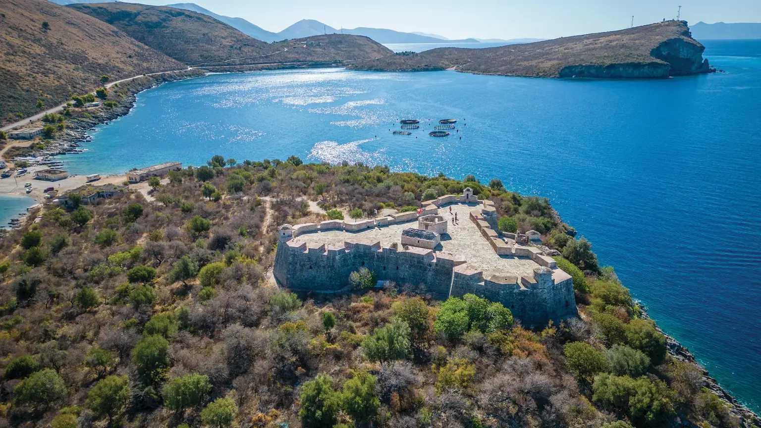 The Castle of Porto Palermo, a triangular Ali Pasha fortress on a small peninsula jutting into the bay, with steep mountains rising behind it