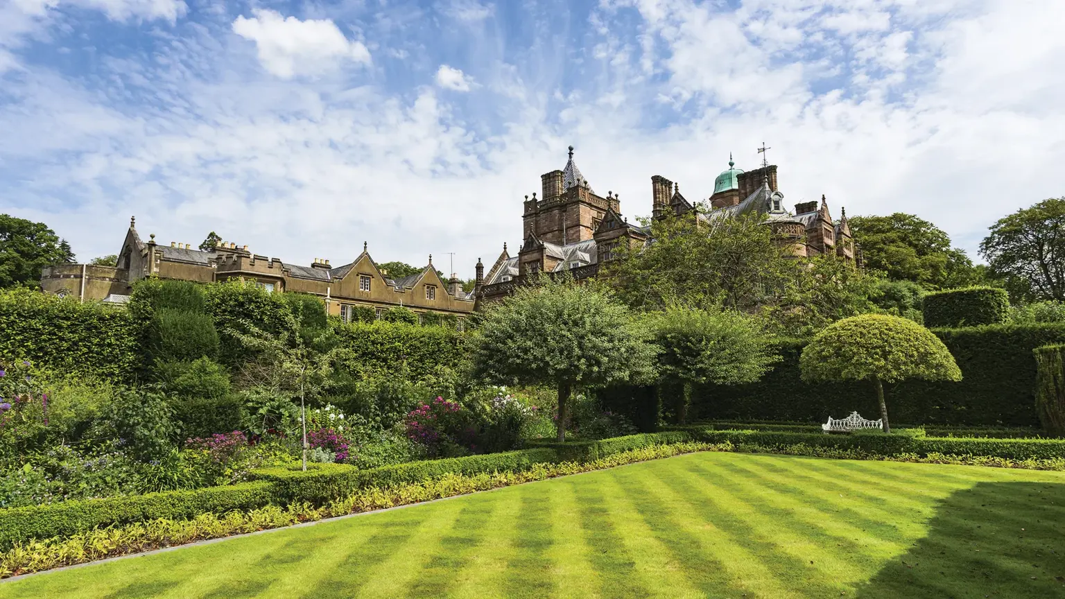 Grand Victorian sandstone country house with ornate chimneys and formal gardens, set against the Lakeland Hills