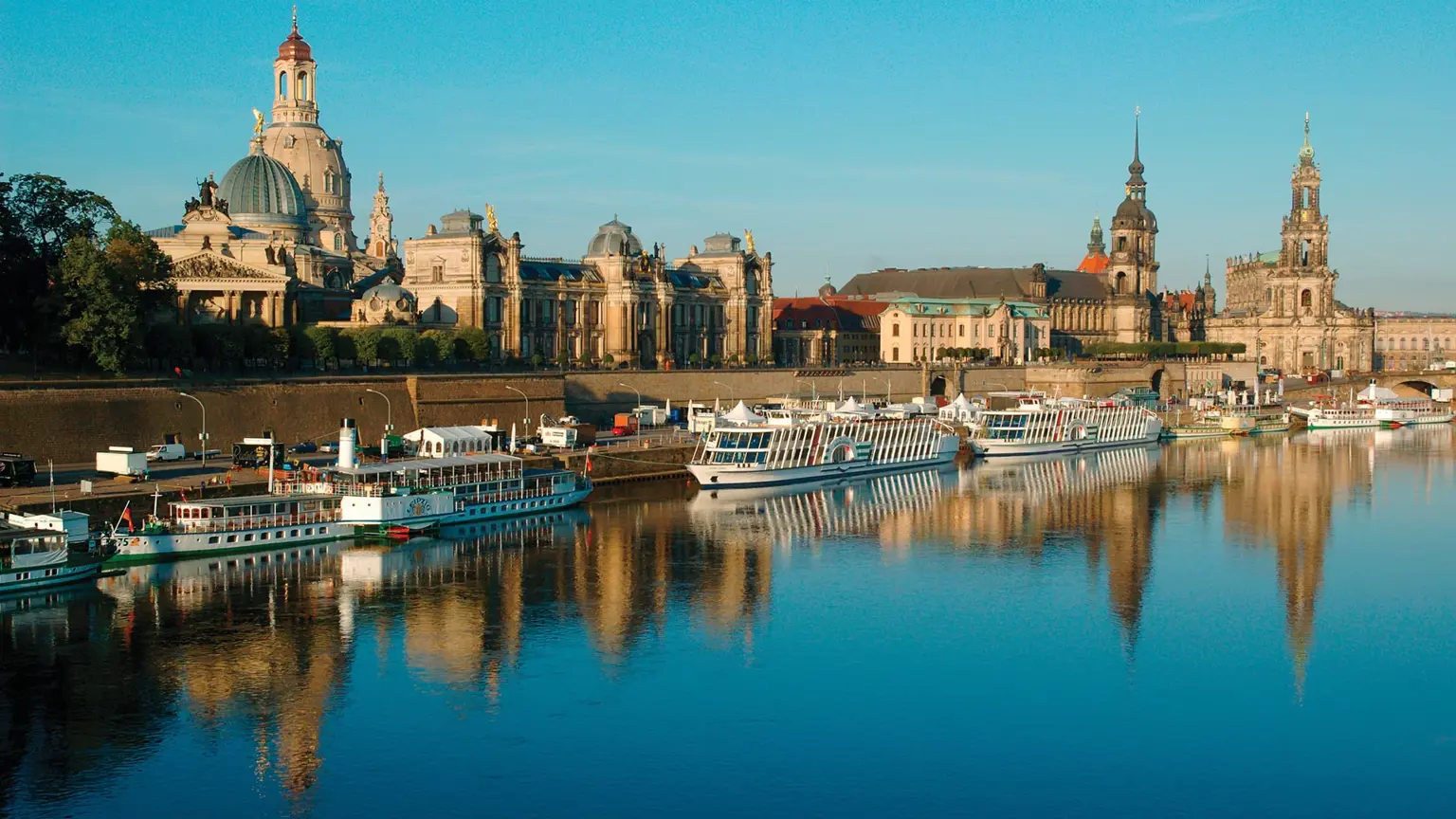 The Dresden old-town skyline of domes and spires reflected in the River Elbe at dawn, with paddle steamers moored along the bank