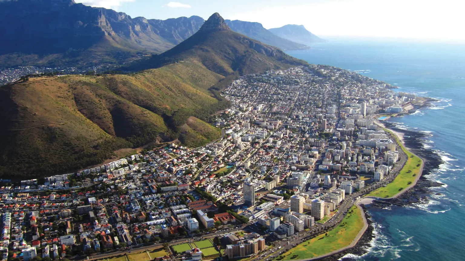 An aerial view of Cape Town spread along the coast beneath Table Mountain and Lion's Head, with the Atlantic seaboard beyond
