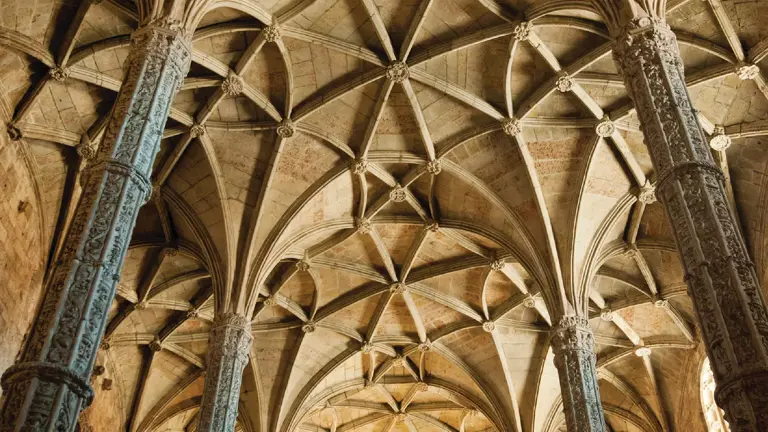 Soaring Manueline vaulted stone ceiling fanning out from carved columns, with a rose window glowing gold at the far end