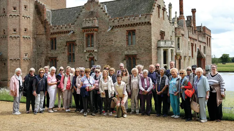 Group of visitors standing outside a large brick manor house with moated grounds on a garden visit.