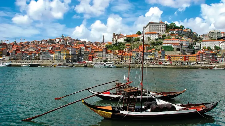 Two traditional flat-bottomed rabelo boats moored on the Douro in front of Porto's stacked, colourful riverside houses