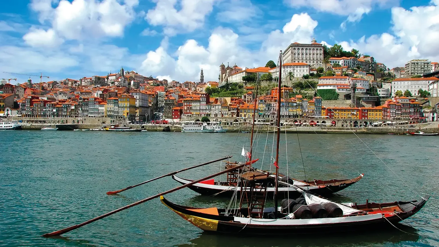 Two traditional flat-bottomed rabelo boats moored on the Douro in front of Porto's stacked, colourful riverside houses