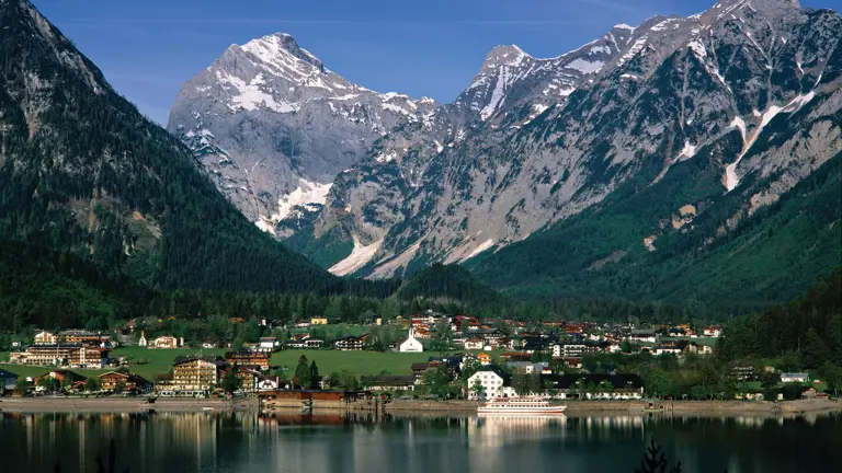The village of Pertisau on the shore of Lake Achensee, its calm water reflecting the steep snow-streaked mountains behind