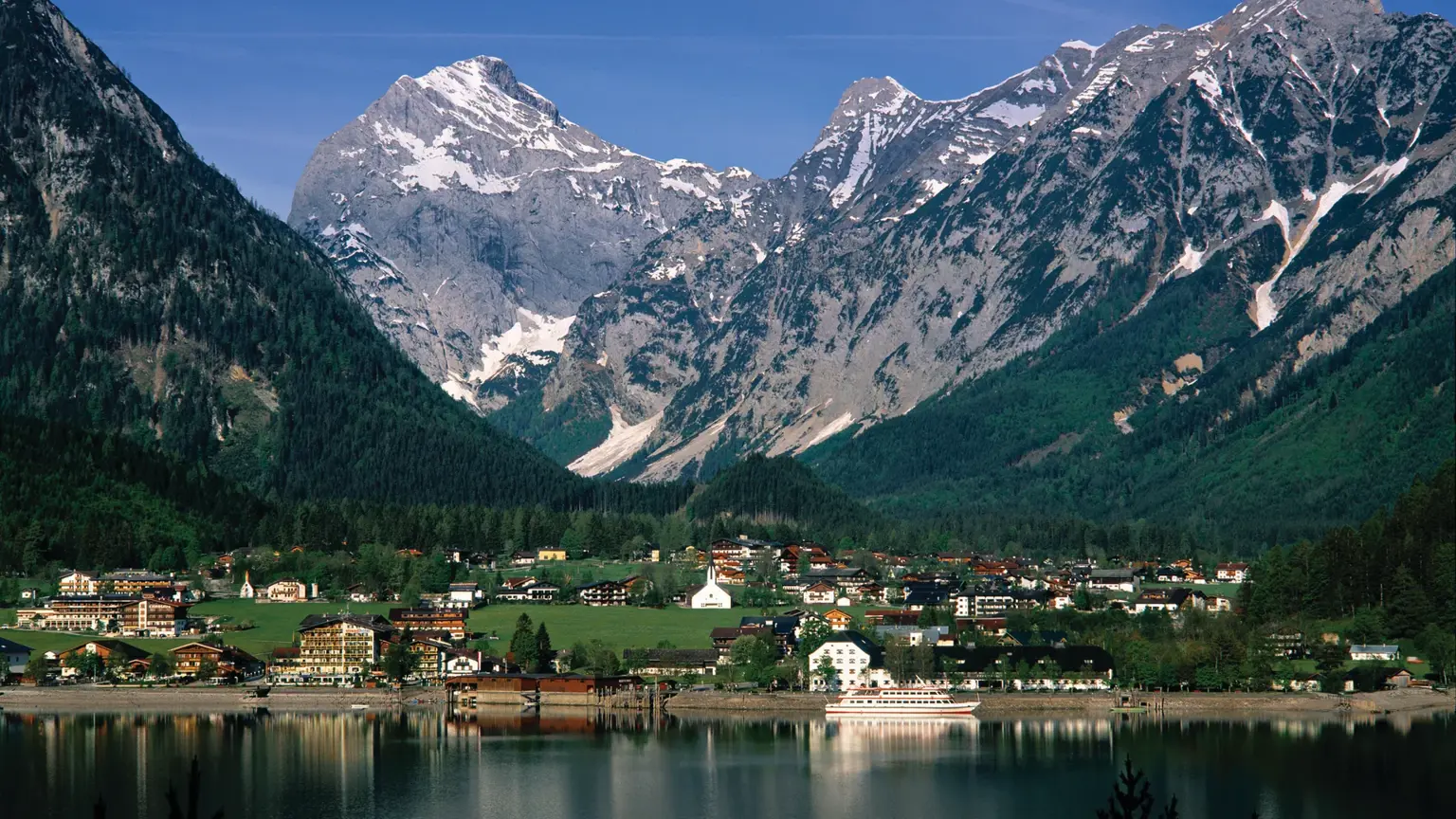 The village of Pertisau on the shore of Lake Achensee, its calm water reflecting the steep snow-streaked mountains behind