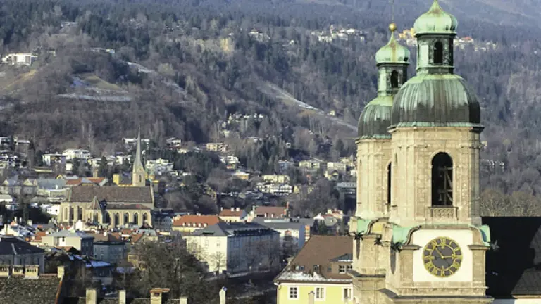 The green-domed cathedral tower rising above the rooftops of Innsbruck, snow-dusted Alpine peaks towering behind