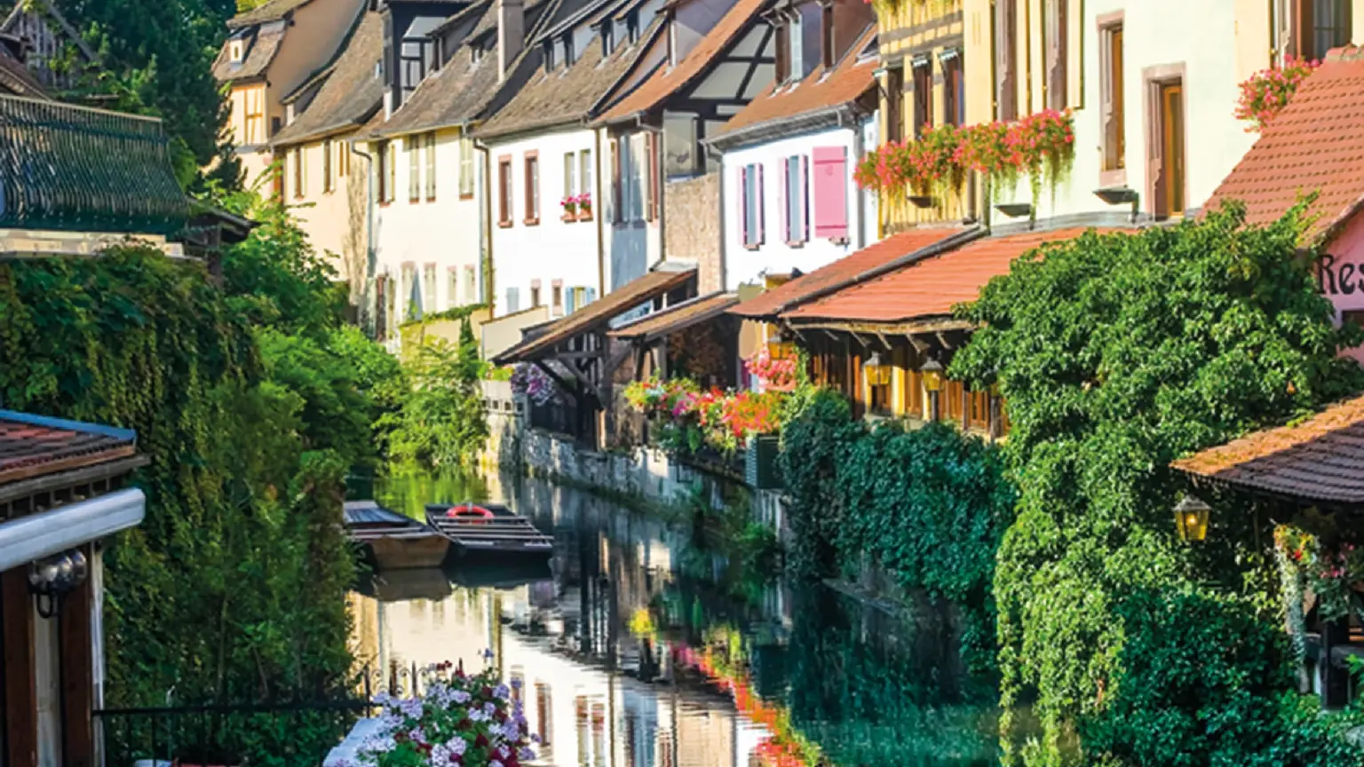 A narrow canal between colourful half-timbered houses with window boxes, reflected in still water.