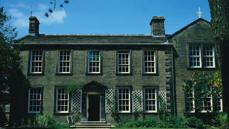 The Georgian stone front of the Brontë Parsonage at Haworth, a symmetrical two-storey house with central porch and trellised windows, the family home of the Brontë sisters