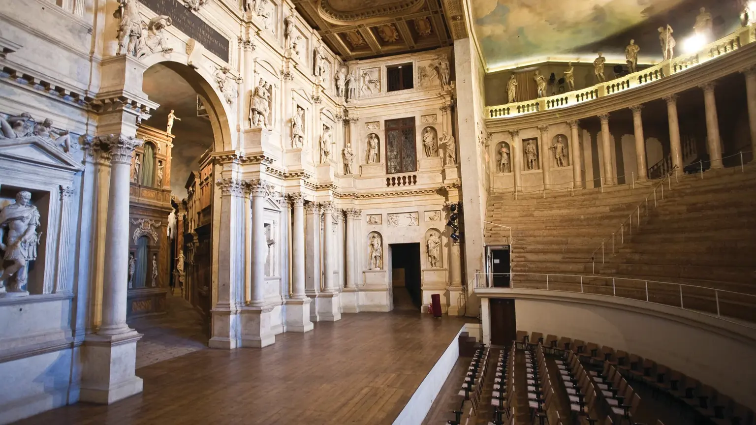 The interior of Palladio's Teatro Olimpico in Vicenza, marble columns and a gilded frescoed ceiling above the wooden seating