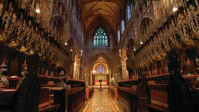 The choir of Chester Cathedral looking east towards the high altar, with elaborately carved 14th-century dark oak choir stalls flanking a tiled aisle and Gothic stone vaulting above
