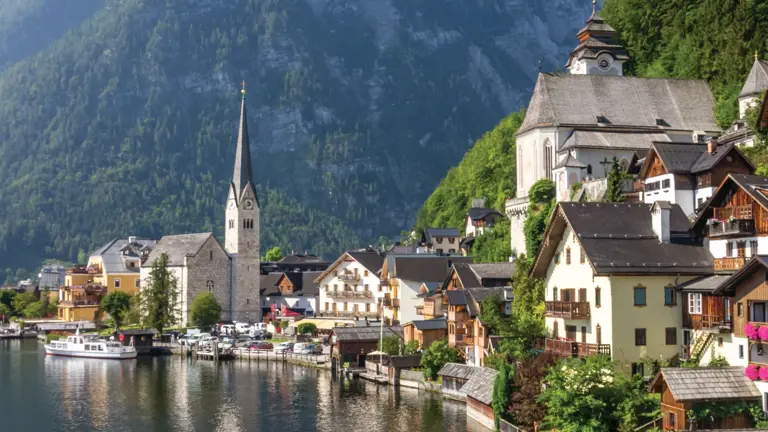 Hallstatt's pastel lakeside houses and church towers reflected in the calm Hallstättersee, mountains rising steeply behind