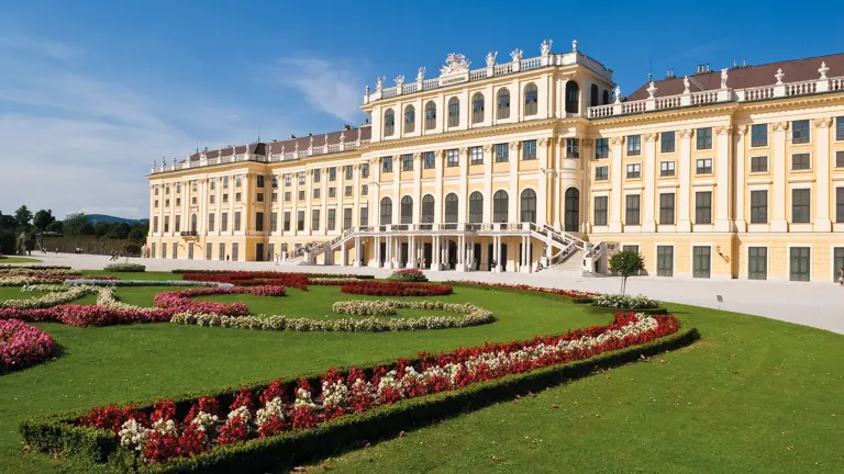 The long yellow garden facade of Schönbrunn Palace behind its formal parterre of red and white flowerbeds and clipped lawns