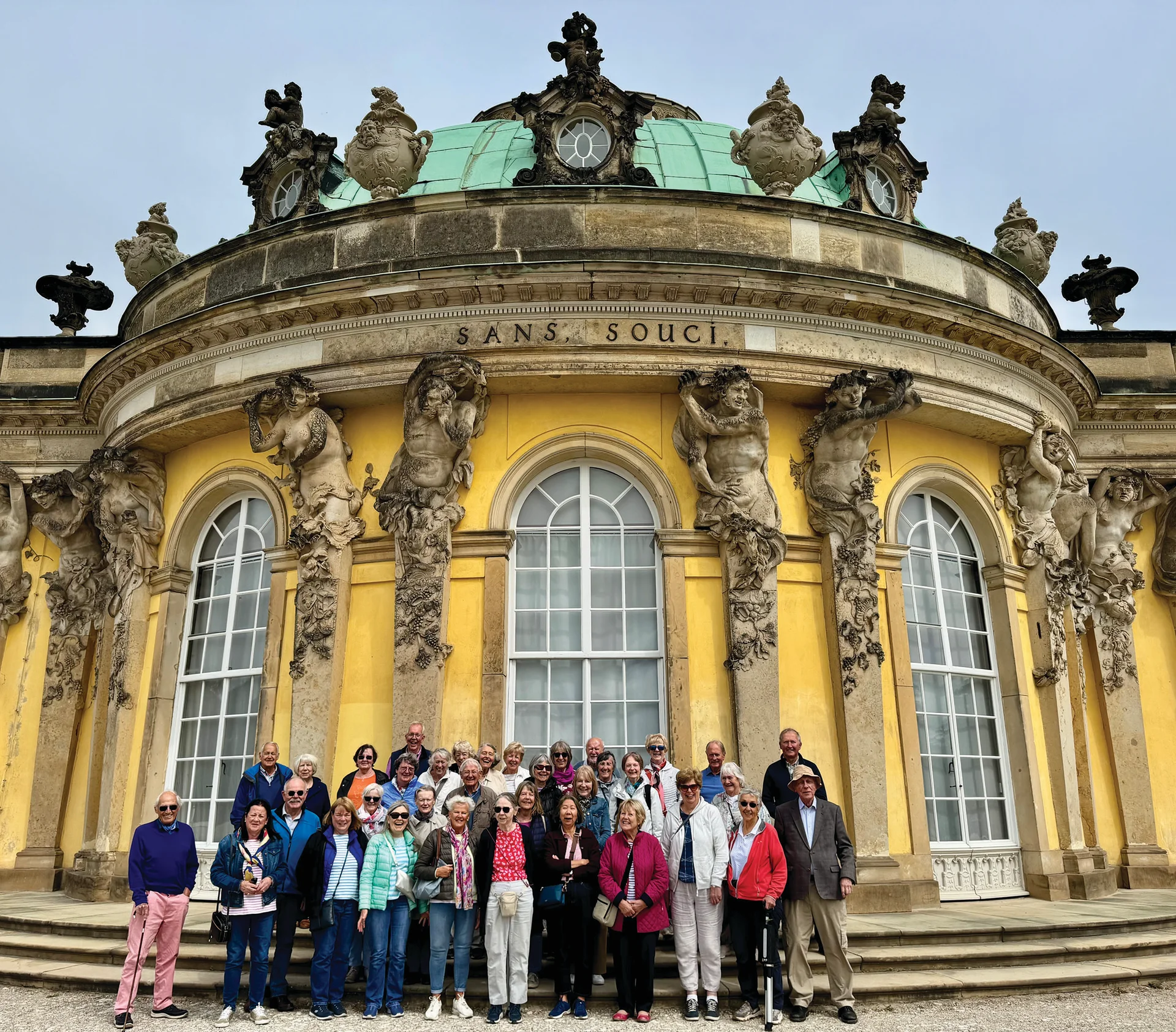 Group of visitors gathered outside Sanssouci Palace, an 18th-century Rococo palace with manicured palace grounds.
