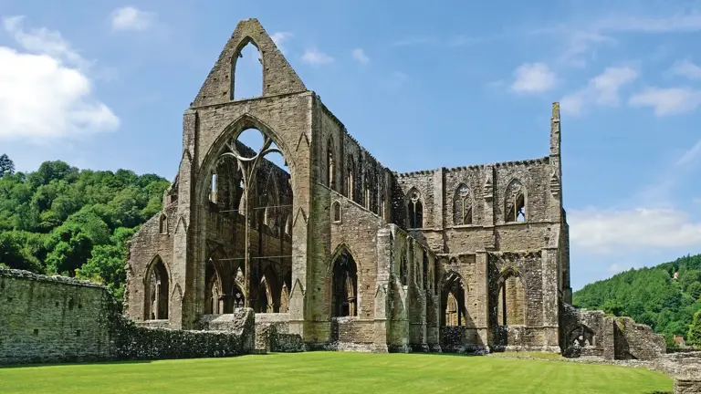 Roofless Gothic shell of Tintern Abbey rising from the green meadows of the Wye Valley, its great pointed-arch windows framing the sky and wooded Monmouthshire hills beyond