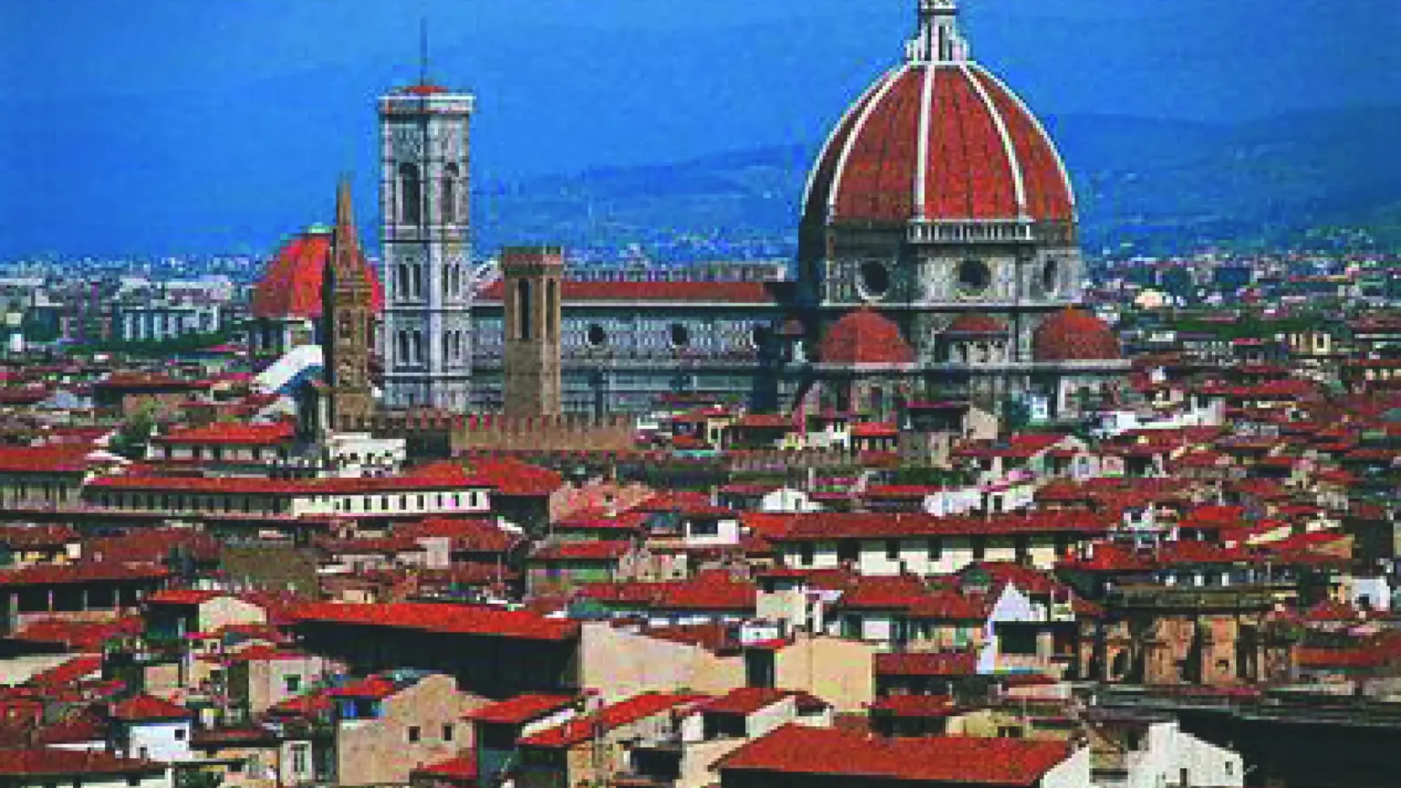 An elevated view of Florence, the red-domed Duomo and Giotto's striped campanile rising above the terracotta rooftops, blue hills beyond