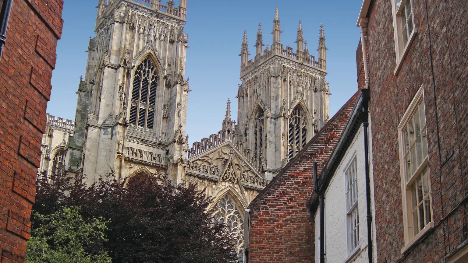 Twin gothic towers and intricate stonework of York Minster framed by red-brick houses and a narrow cobbled street
