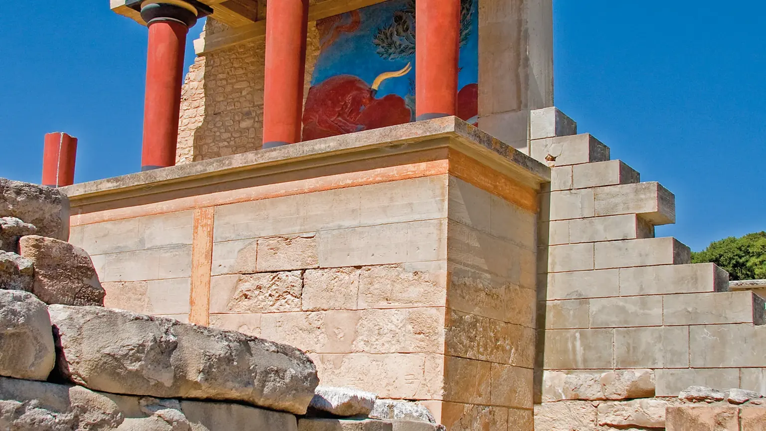 The reconstructed north entrance of the Palace of Knossos, its distinctive tapering red columns and the charging bull fresco above the stonework