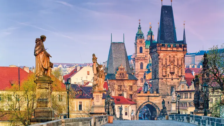 The statue-lined Charles Bridge over the Vltava at dawn, looking towards the Lesser Town bridge tower and Prague Castle beyond