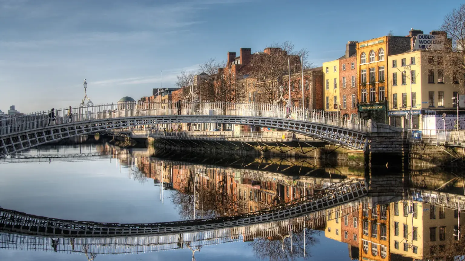 The white cast-iron Ha'penny Bridge arching over the River Liffey, Georgian quayside buildings mirrored in the still water beyond