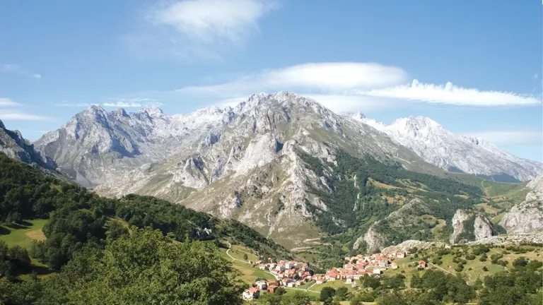 The jagged limestone peaks of the Picos de Europa rising above a green valley with a small village nestled below