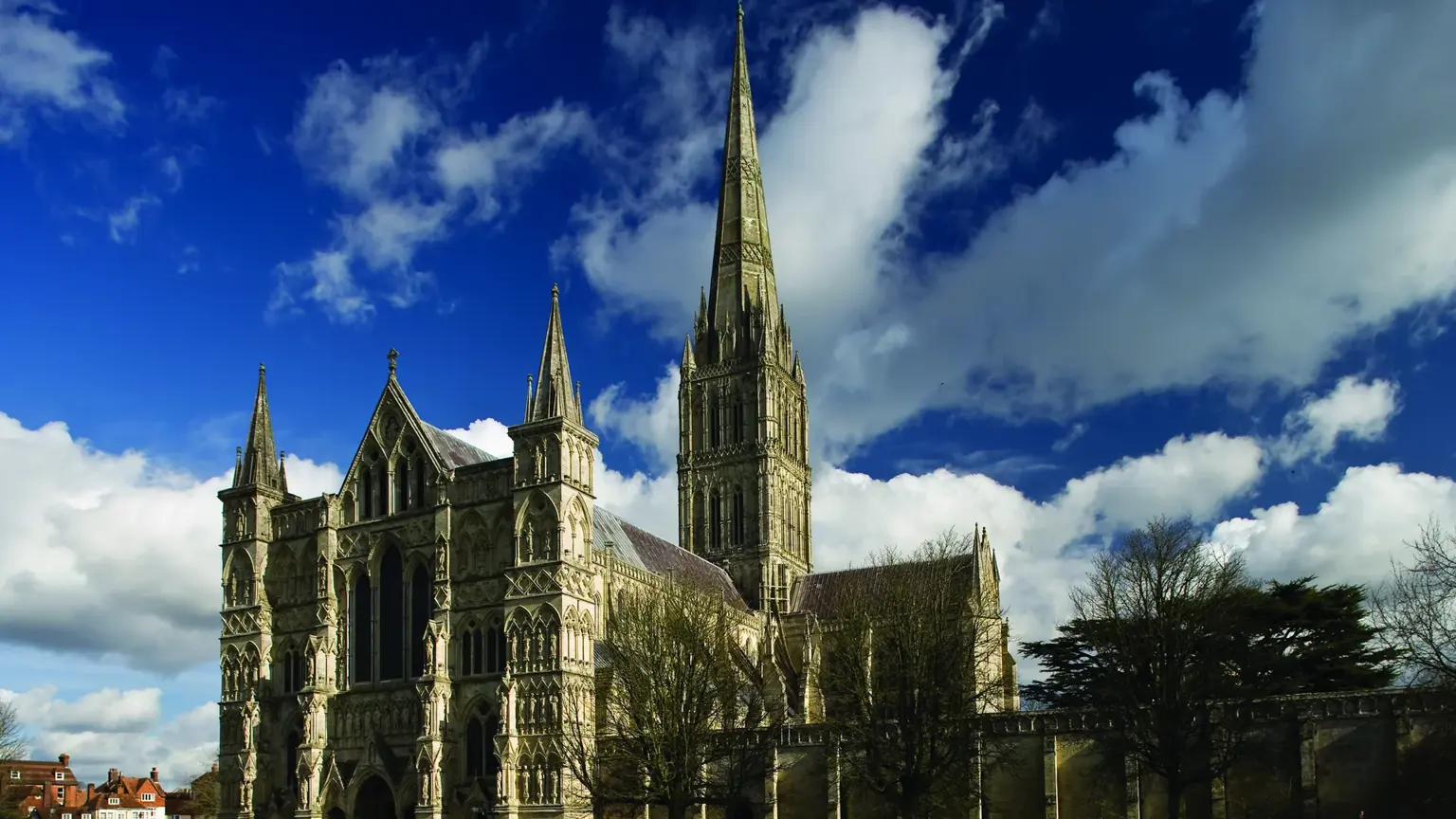 Salisbury Cathedral seen from across a lawn, with the slender 123-metre spire rising against a deep blue sky scattered with clouds