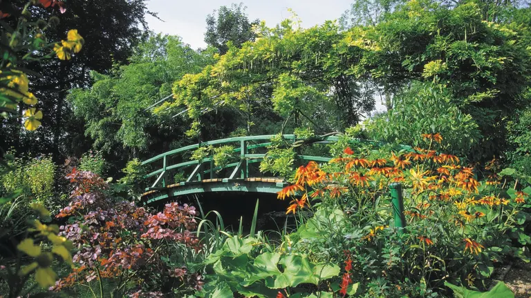 A green Japanese bridge draped in foliage above a riot of orange and pink flowers.