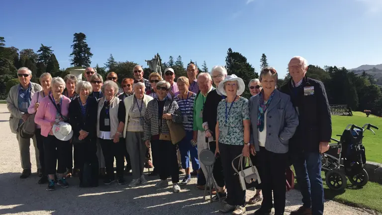 Group of visitors at Powerscourt House and Gardens, County Wicklow, Ireland, with formal gardens and historic mansion visible.