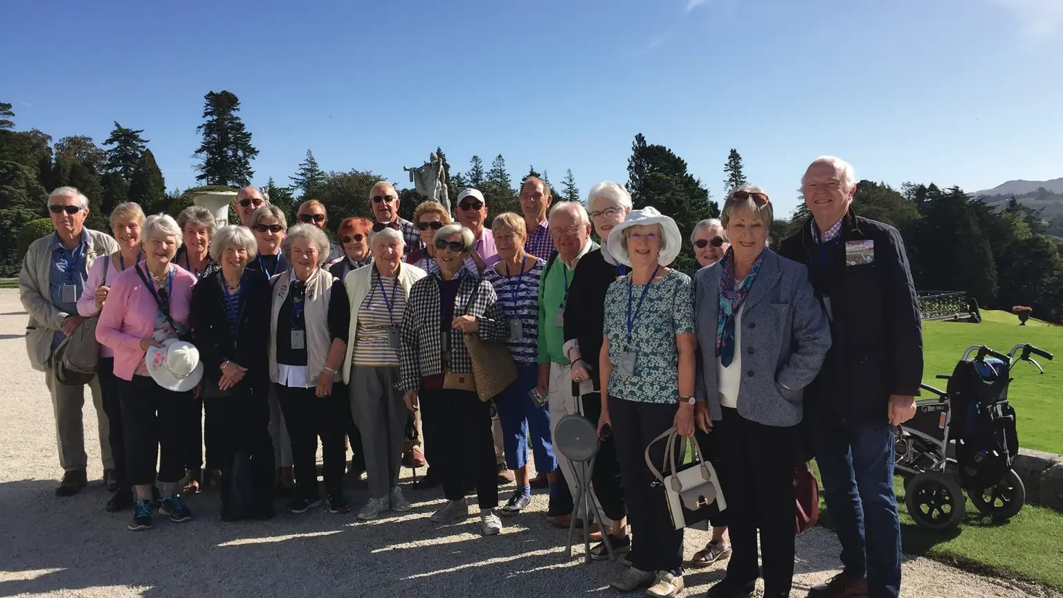 Group of visitors at Powerscourt House and Gardens, County Wicklow, Ireland, with formal gardens and historic mansion visible.