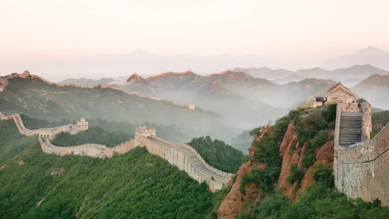 The Great Wall of China snaking along forested ridgelines into misty mountains at dawn