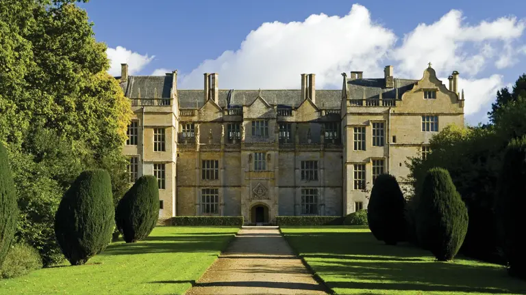 Honey-coloured Elizabethan facade of Montacute House framed by clipped yew topiary along a sunlit lawn