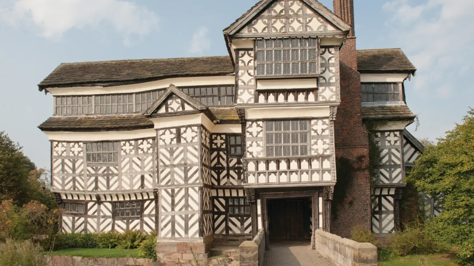 Striking black-and-white timber-framed Tudor moated manor house with crooked walls and small leaded windows