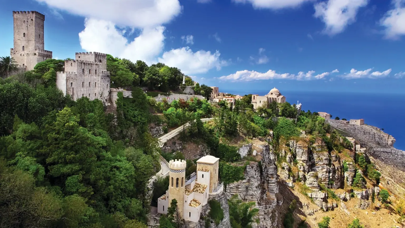 The medieval Sicilian hill town of Erice on its crag, stone houses and church towers above a steep wooded slope with views over the Mediterranean