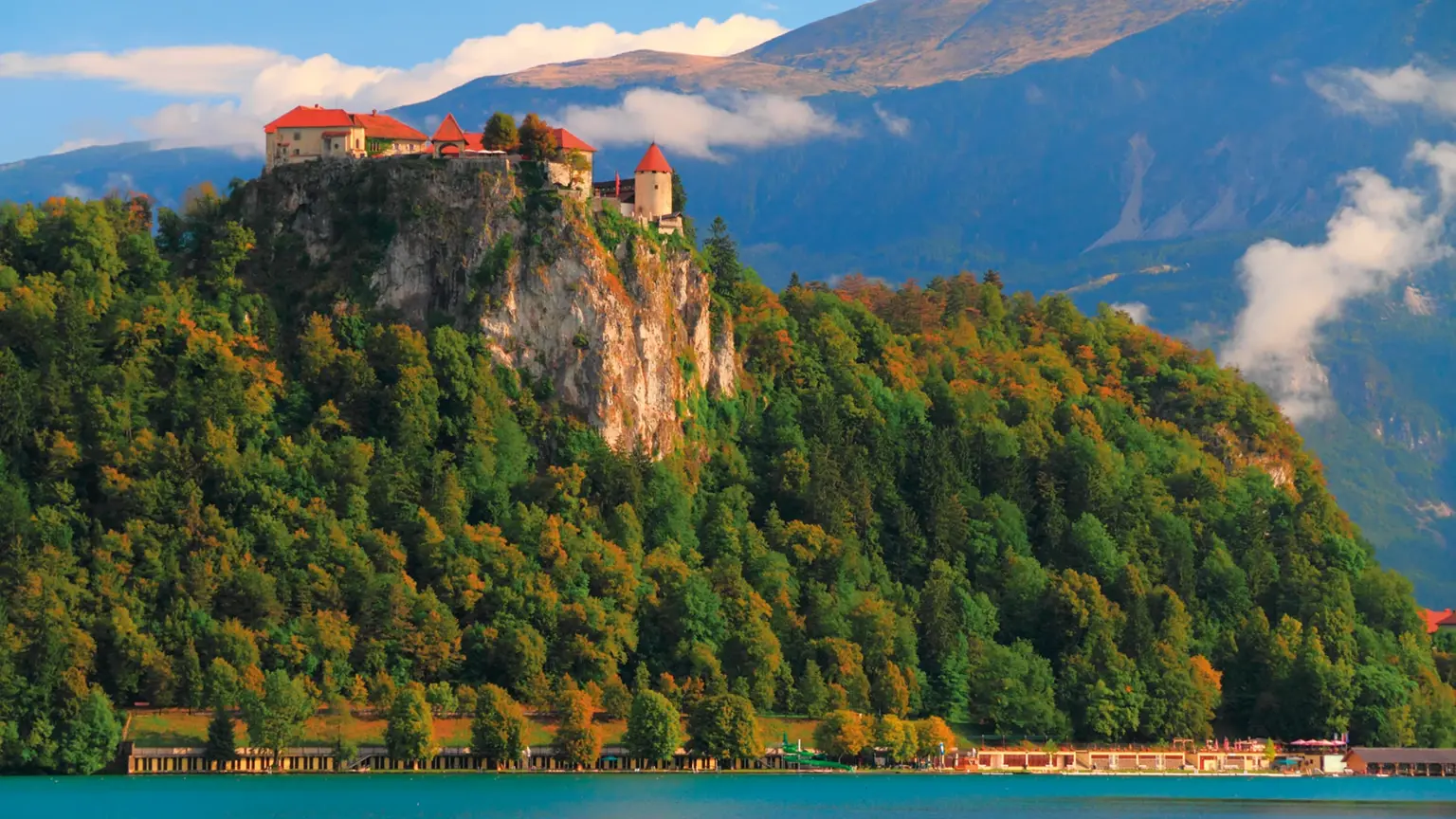 Bled Castle perched on a sheer cliff above the turquoise waters of Lake Bled, with mountains beyond