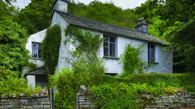 Whitewashed slate-roofed cottage in Grasmere, surrounded by stone walls and lush English garden, the home of poet William Wordsworth