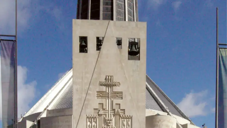 Modernist circular cathedral with a crown of slim spires and a tall stone porch decorated with a relief cross