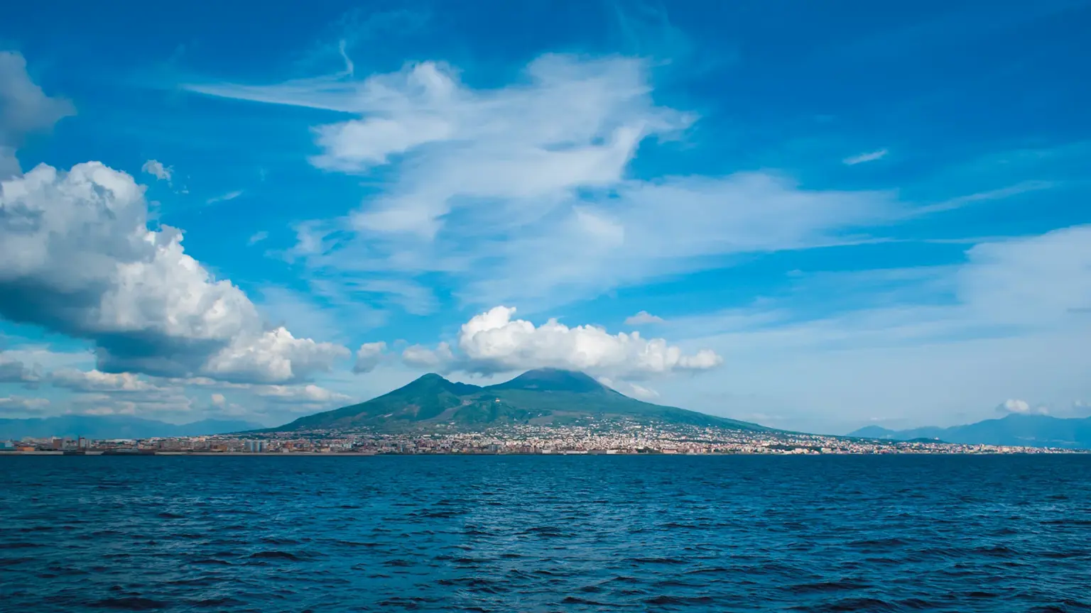 The symmetrical cone of Mount Vesuvius rising beyond the Bay of Naples, the city spread along the shoreline