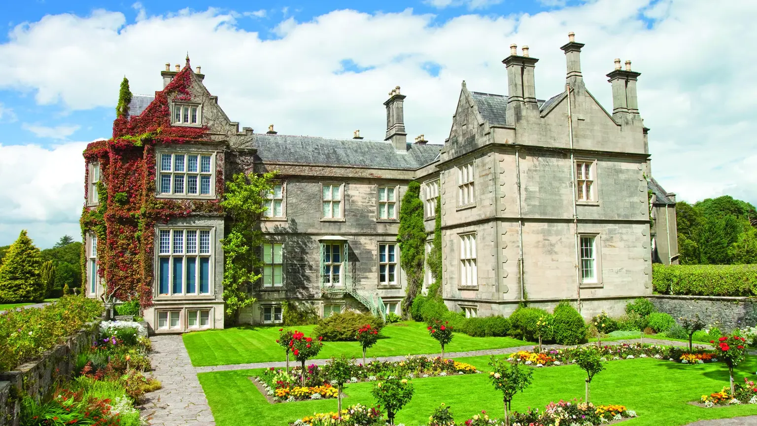 The grey Victorian gables of Muckross House clad in red Virginia creeper, rising above a formal flower garden in Killarney National Park