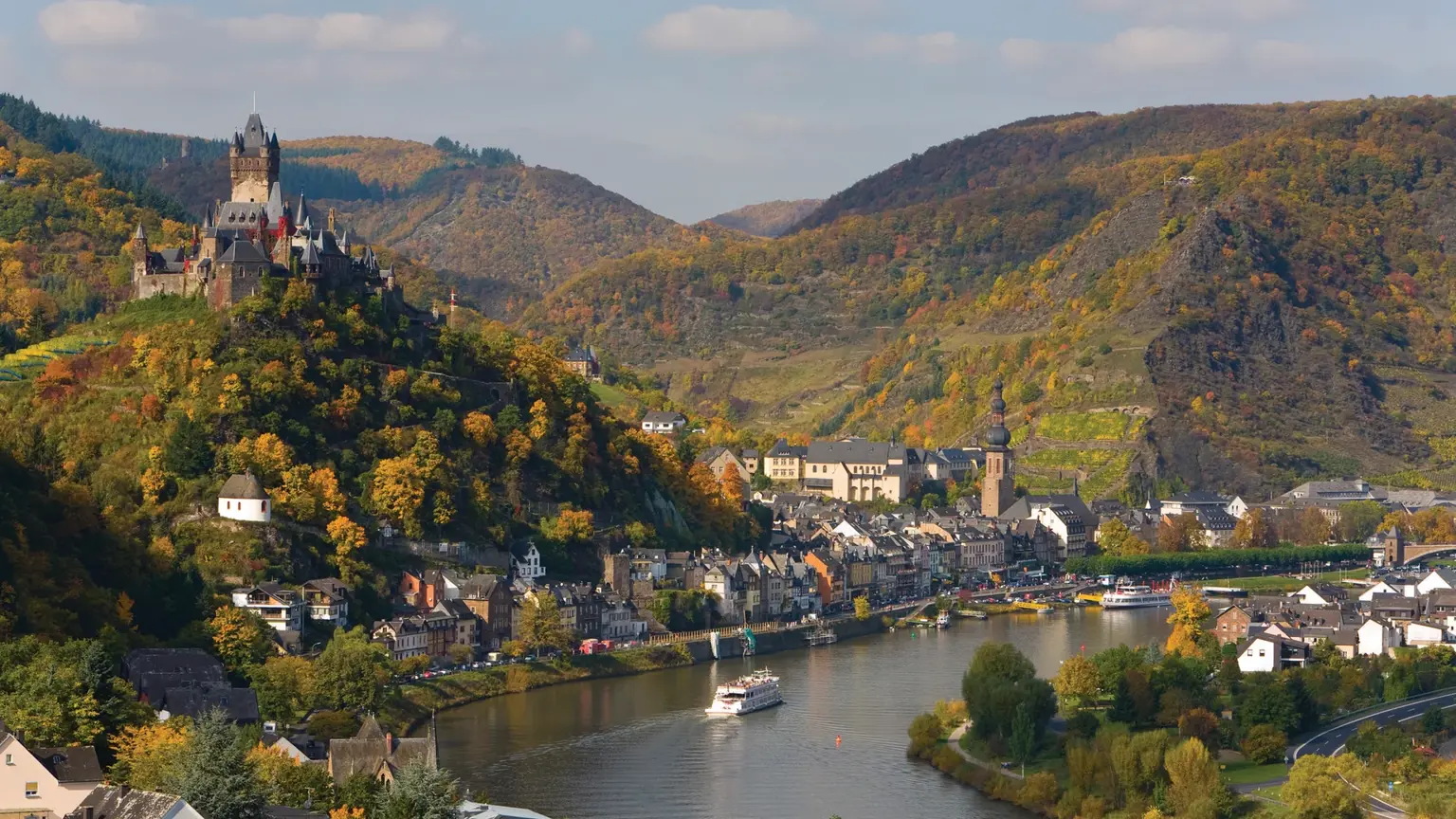 The town of Cochem on a bend of the River Moselle in autumn, the Reichsburg castle rising on a wooded hill above the rooftops