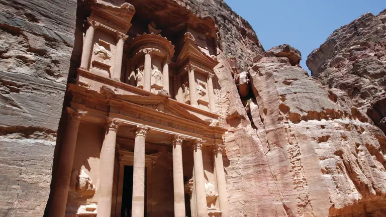 The rose-red carved facade of the Treasury (Al-Khazneh) at Petra, framed by the towering walls of the sandstone gorge