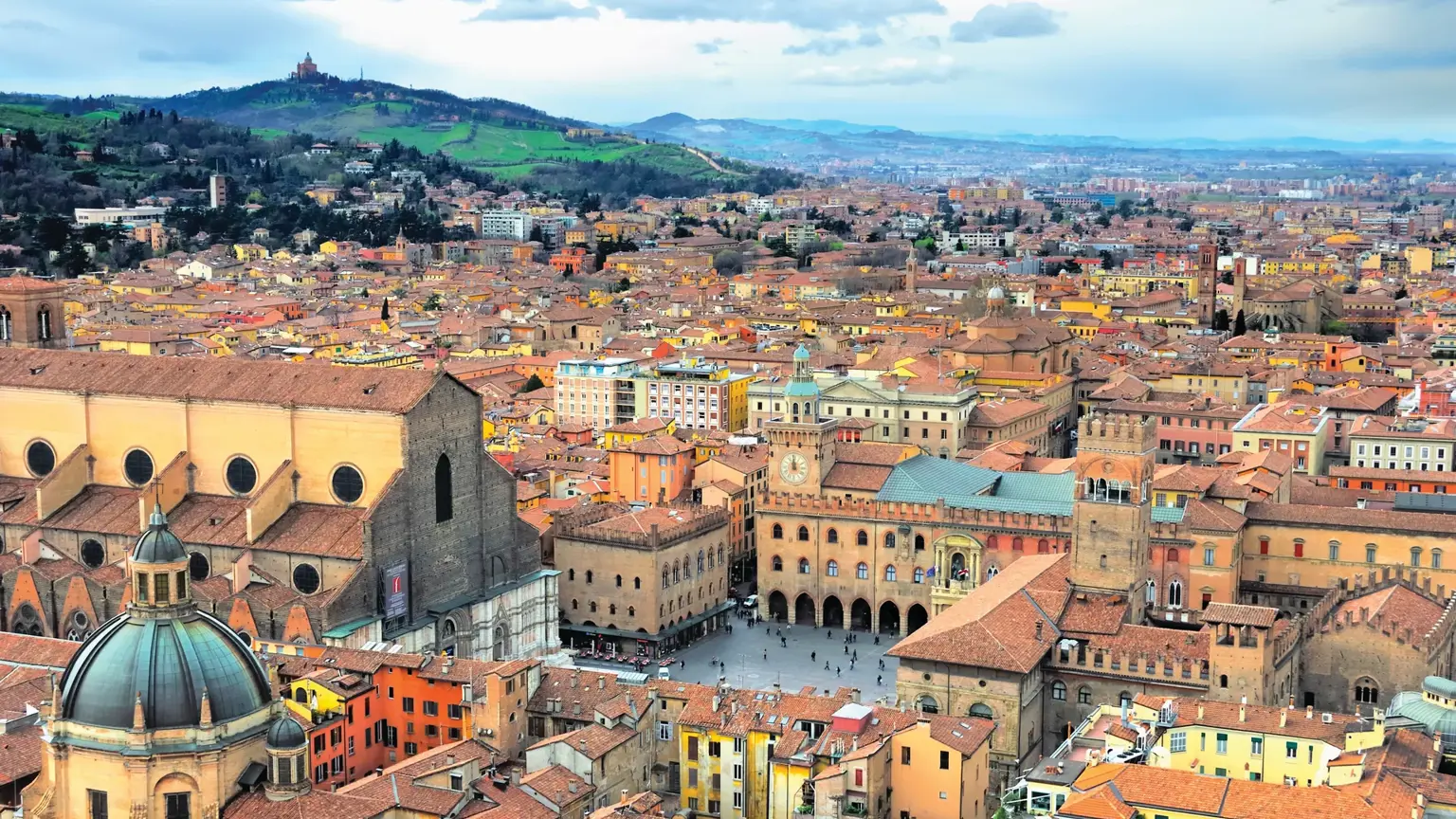 An aerial view across the terracotta rooftops of Bologna to the leaning Asinelli and Garisenda towers above the medieval city