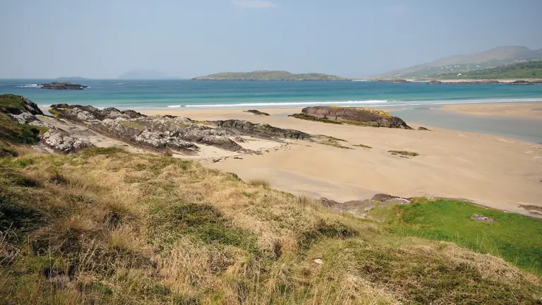 A wide curve of white sand and turquoise shallows on the Ring of Kerry coast, green headlands and islands stretching into the distance
