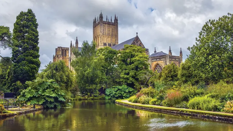 Wells Cathedral's central tower rises above lush gardens reflected in the still water of the Bishop's Palace moat