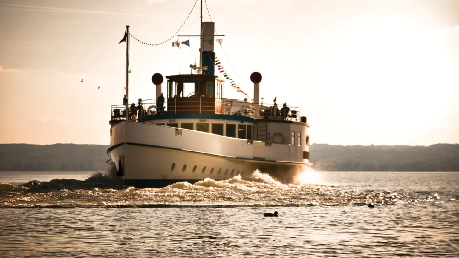A bunting-decked vintage paddle steamer crossing the calm waters of Lake Ammersee in golden evening light
