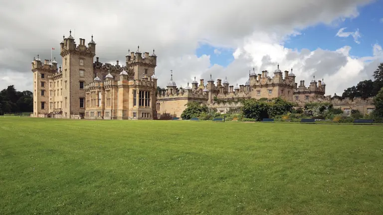 The vast turreted and pinnacled facade of Floors Castle at Kelso, the seat of the Duke of Roxburghe, stretching across a sweeping green lawn under a Scottish sky